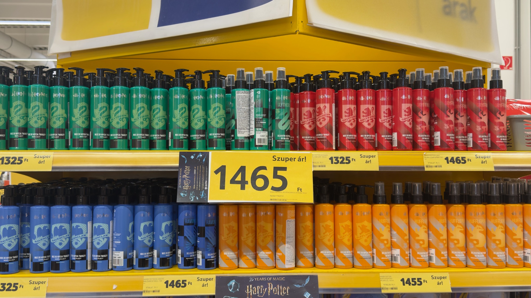 Harry Potter-termékek polca a négy roxforti ház színeivel: pumpás arctisztító mousse-ok és mellettük hajápoló spray-k.