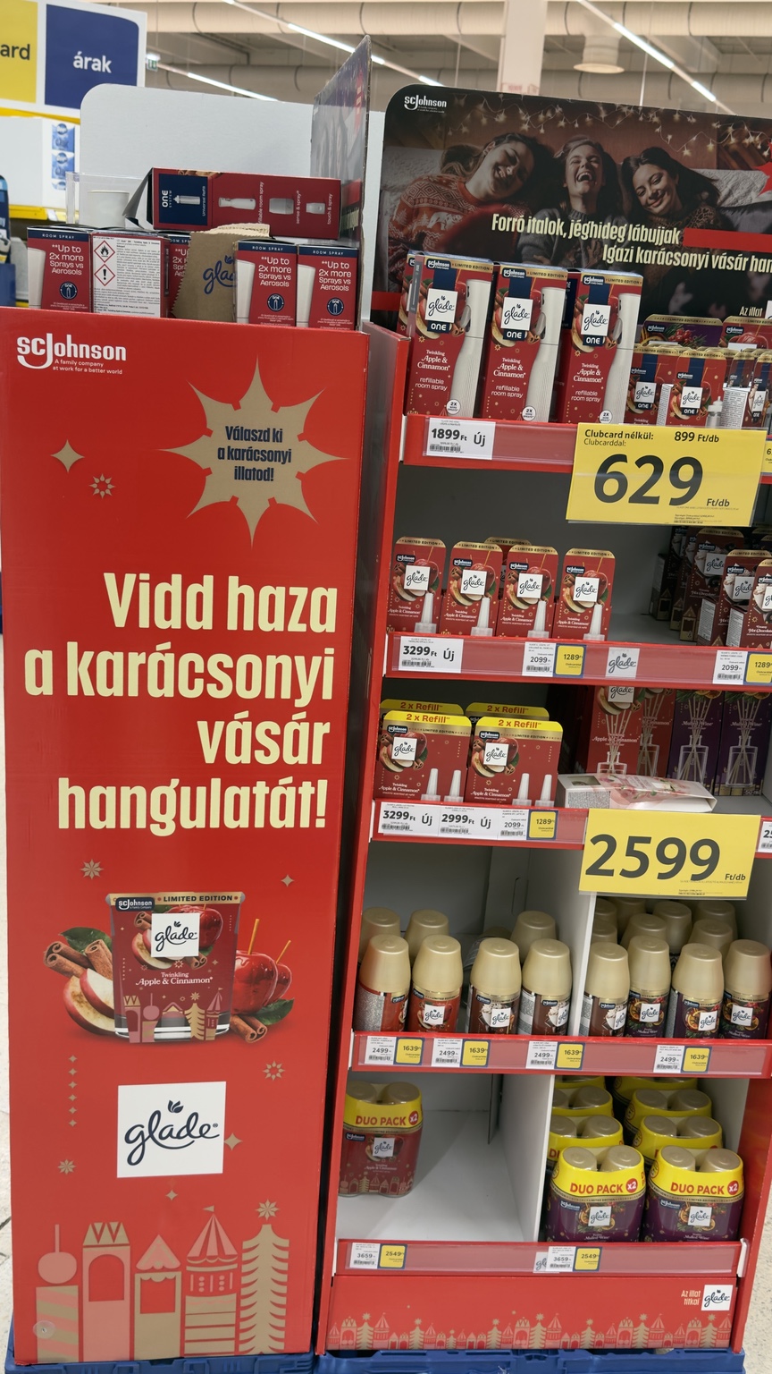 Piros Glade-állvány karácsonyi vásárt idéző grafikával, almás-fahéjas termékekkel és sárga Clubcard-árkártyákkal.